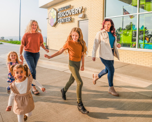 Two women and three young girls happily strolling outside of the Magic City Discovery Center