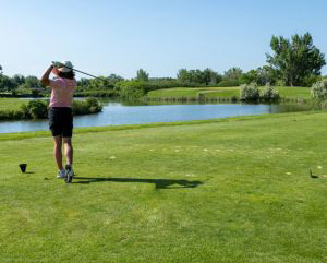 View from behind of a golfer teeing off with greenery and a pond surrounding them