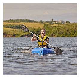 A woman kayaking on a lake with a hilly landscape in the background