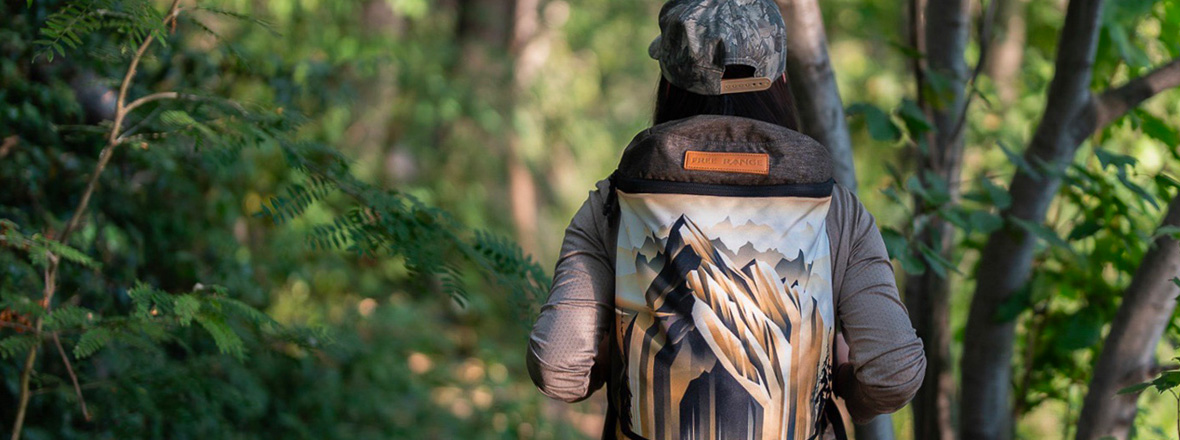 A canvas outdoor backpack with artwork of a mountain being worn by a person.