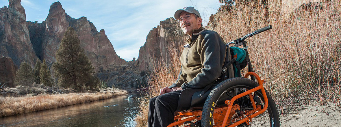 A man in a specialized wheelchair with an extra wheel in front for maneuverability.