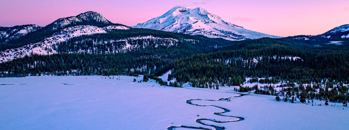 A snow-peak mountain over a windy snow covered river.