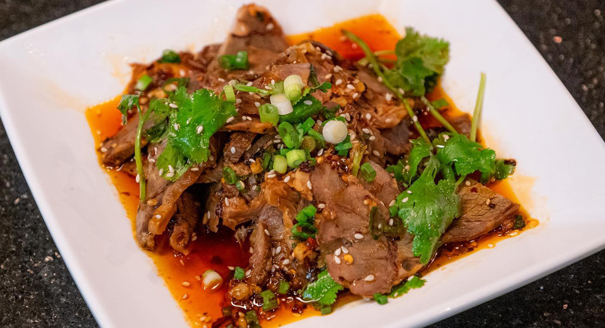 Meat, sauce, green onions and cilantro on white square-shaped plate.