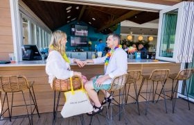 Two people sitting at an outdoor bar, wearing colorful leis.