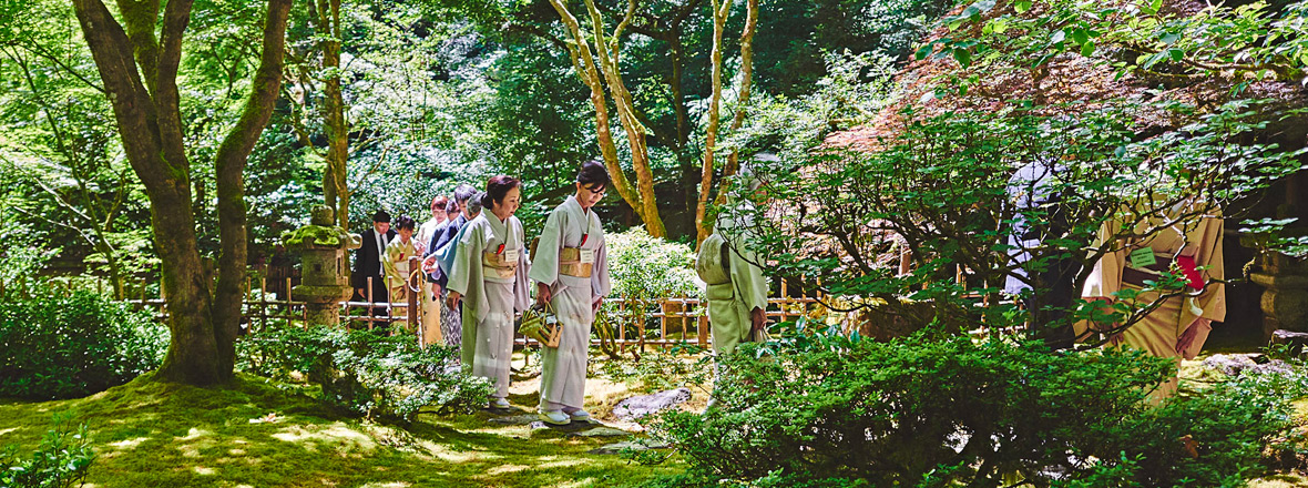 People stand in a garden with a bridge in the background.