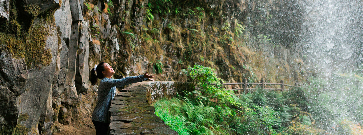 A person reaches out to a waterfall flowing overhead.
