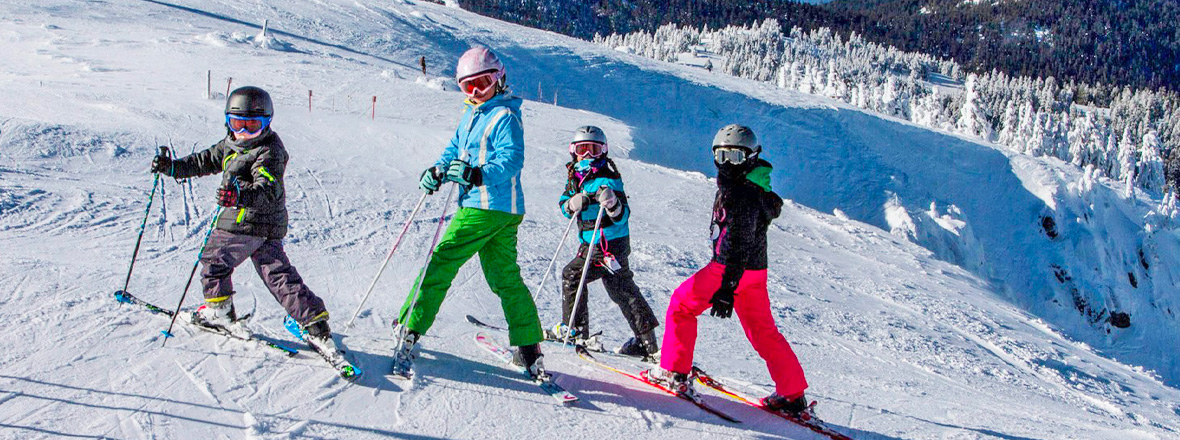 An adult and three children pose on their skis on a snowy ski trail.