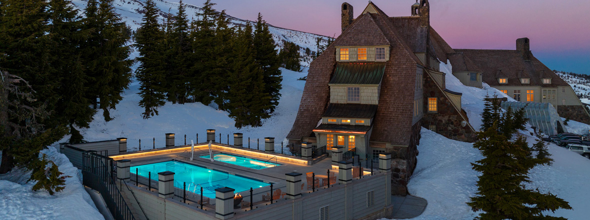 A snowy mountain scene with Timberline Lodge in the foreground, surrounded by a winter landscape.