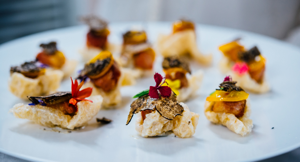 Elegant bite-sized appetizers on a white plate, featuring puffed bases topped with truffle shavings and edible flowers.