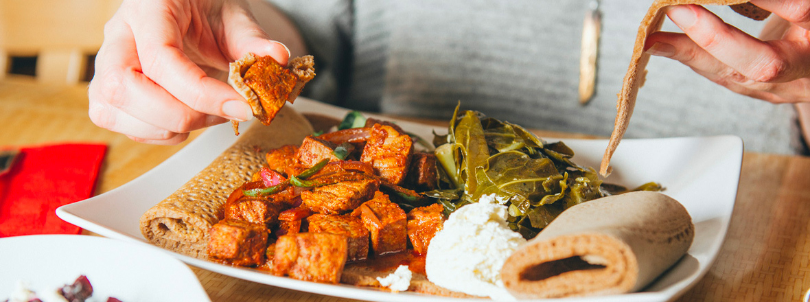 A plate of Ethiopian food, including collard greens, soft cheese, stewed chicken and injera, a type of flatbread.
