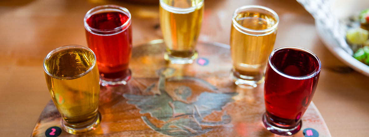 A flight of a variety of ciders in pint glasses.