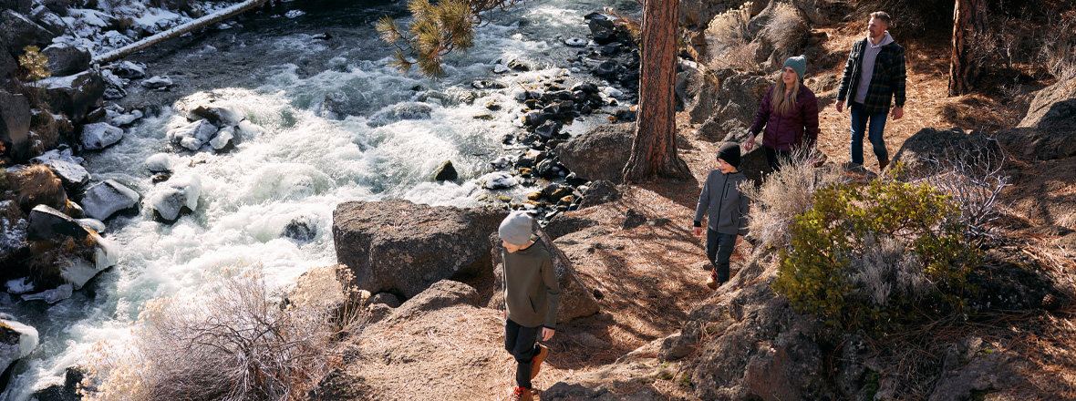 A family of 4 hiking along a trail next to a rushing river.