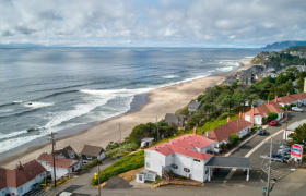 Aerial view of a coastal town with red-roofed buildings and a beachside motel overlooking a wide sandy shoreline and the ocean.