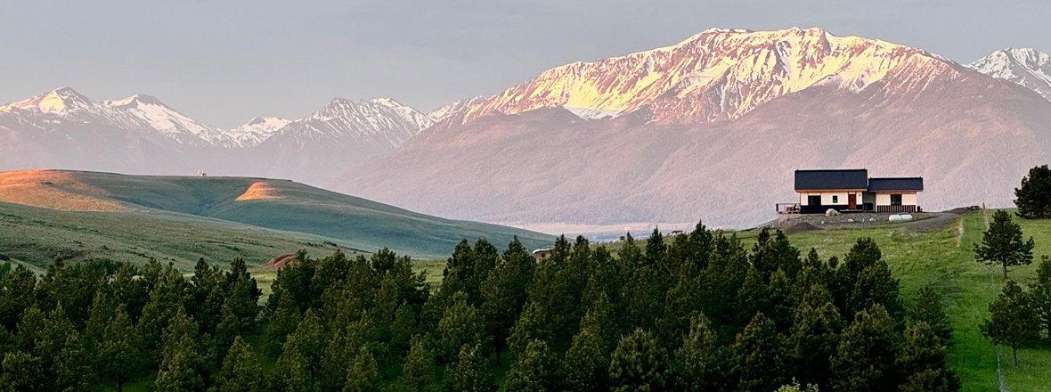 Landscape of hills, firs, mountains and a lone Japanese-style home in the distance.