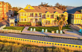 Beachfront inn with Adirondack chairs on the lawn, glowing in the golden light of sunset and facing a seaside promenade.
