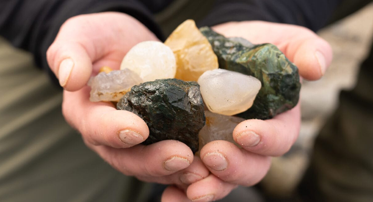 Hands hold a collection of shiny colorful rocks.