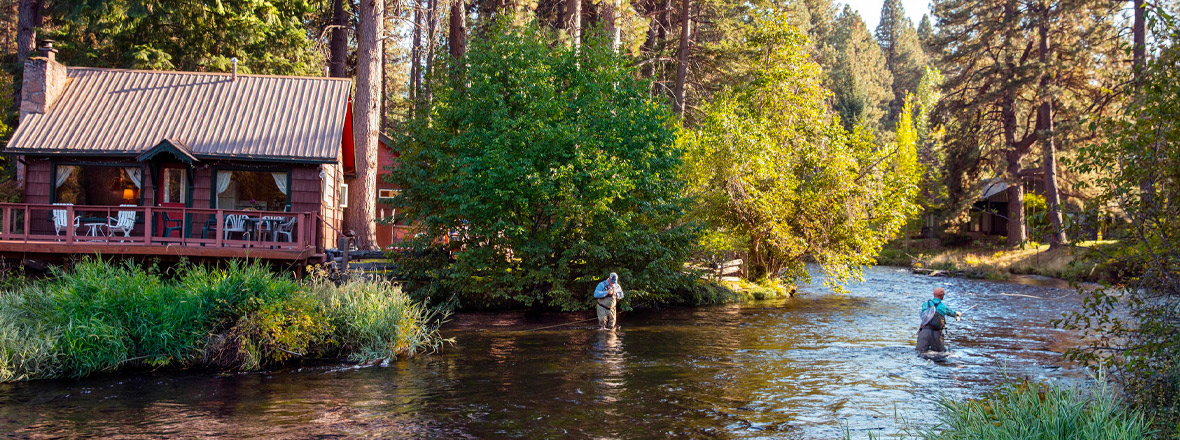 Two people standing in a river cast lines for fly-fishing.
