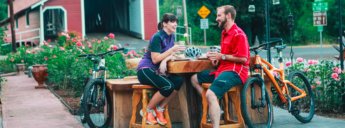 Two mountain bikers take a break for beers in front of the iconic red Office Bridge in Westfir.