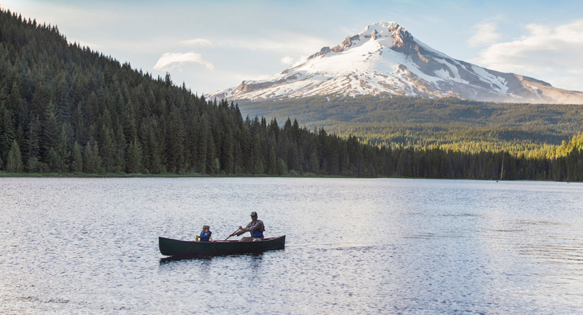 An adult and child canoe in a Mt. Hood-reflected lake.