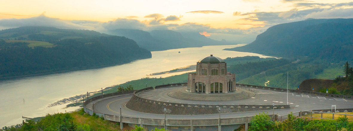 A historic stone building sits high on a bluff overlooking a river.