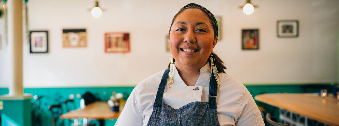 An indigenous woman stands inside a restaurant.