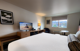 Cozy hotel room with a king-size bed, flat-screen TV, lounge chair, and window overlooking a scenic town view.