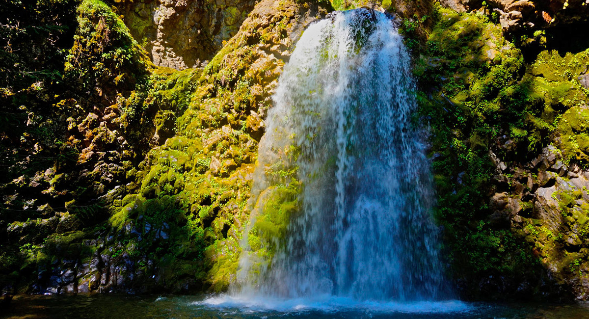 A tall waterfall against a mossy cliff.
