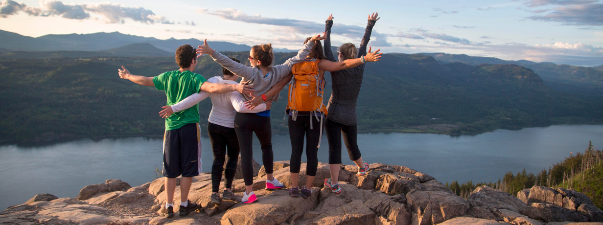 A group of people with their arms extended taking in the view of the Columbia River from a tall peak.
