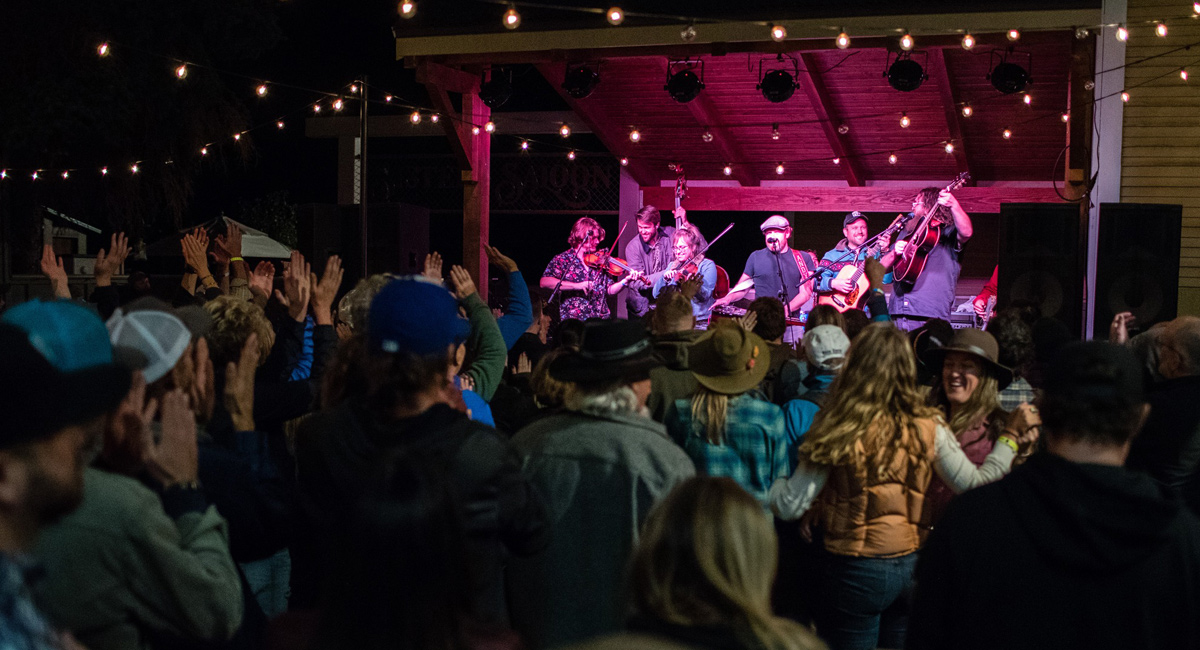 A crowd watches and dances as a live band plays on a small stage.