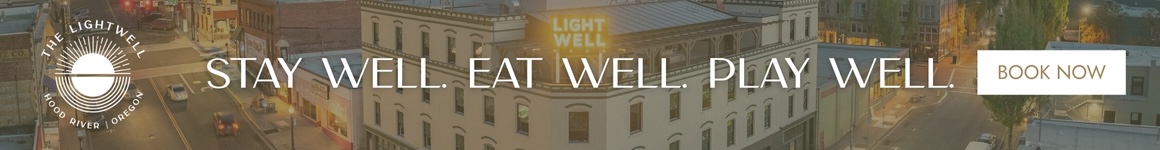 Banner for The Lightwell hotel in Hood River, Oregon, showing a view of the historic downtown building at dusk with glowing signage and the slogan “STAY WELL. EAT WELL. PLAY WELL.