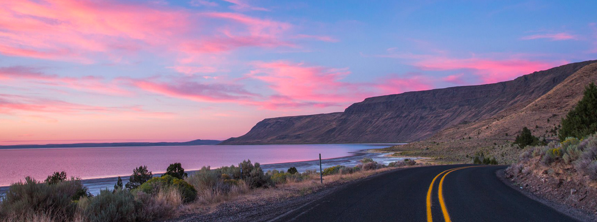 A pink and blue sunset on a long stretch of backcountry road.