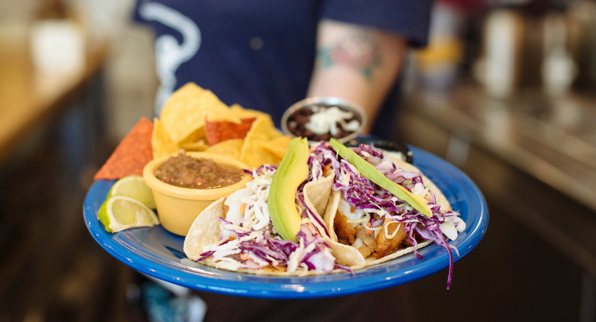 A plate of fish tacos with a side of chips and salsa.