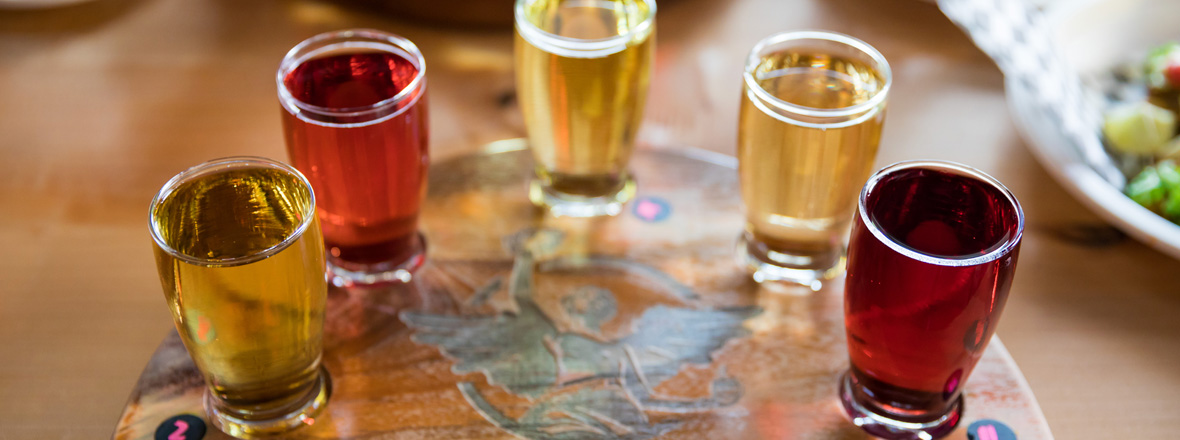 A flight of five ciders served on a wooden board.