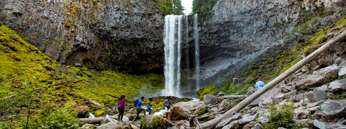 Hikers are in the foreground of a tall waterfall.