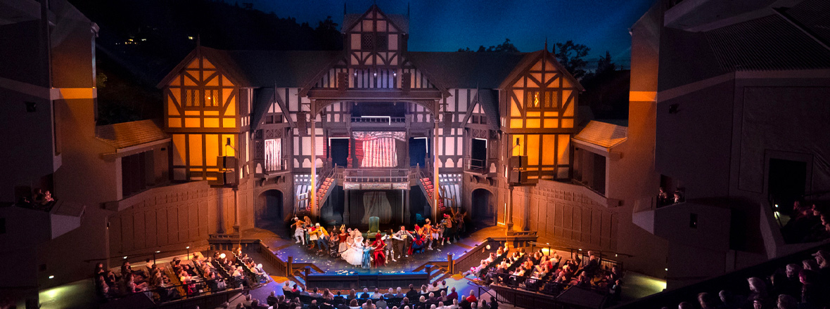 A play performed in an outdoor stage, with the backdrop set of a old English style building.