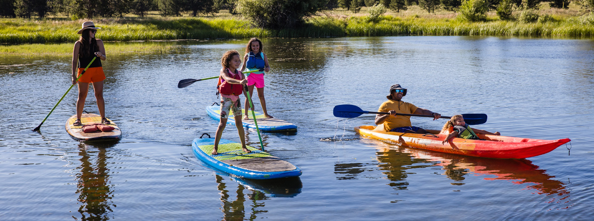 Three people paddle on stand-up paddleboards while a man and a dog paddle alongside in a kayak.