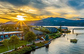 Sunset over Hood River waterfront with mountains, a hotel, and a dock.