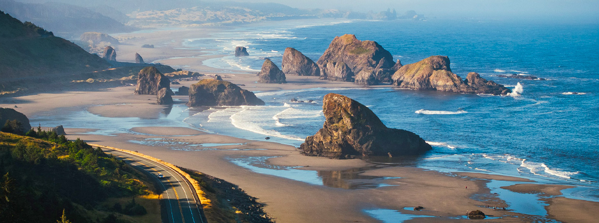 An aerial view of a road winding next to ocean sea stacks.