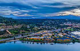 Aerial view of a riverside town at sunset with Mount Hood in the distance.