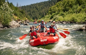 People whitewater rafting on a scenic Oregon river surrounded by lush forest under a clear blue sky.