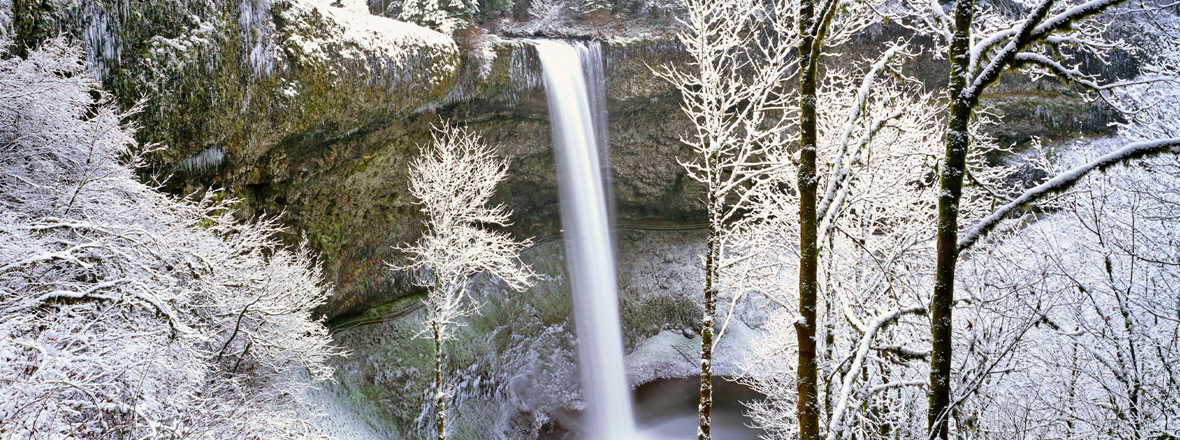Snow surrounds a tall waterfall.