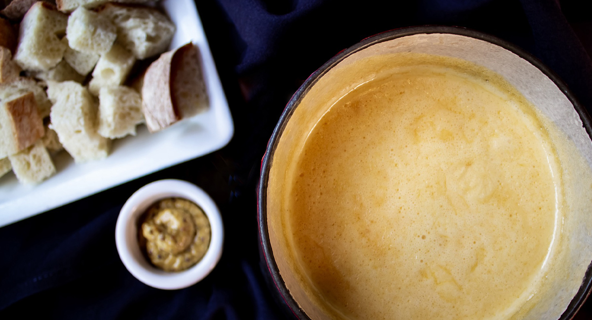 Overhead view of a pot of melted fondue cheese and sides.