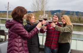 Four people clinking glasses of red wine outdoors on a patio, smiling and enjoying each other's company.