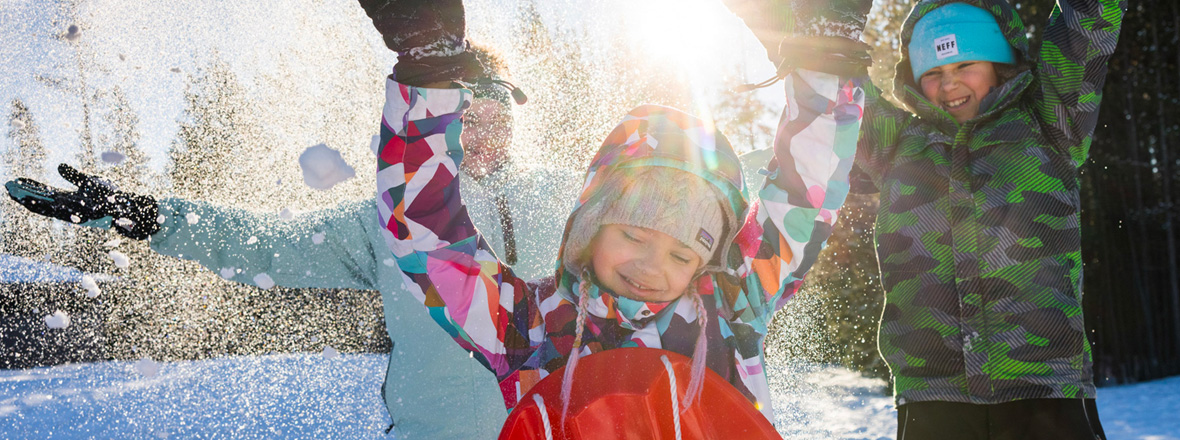 Children smiling and throwing snow in the air.
