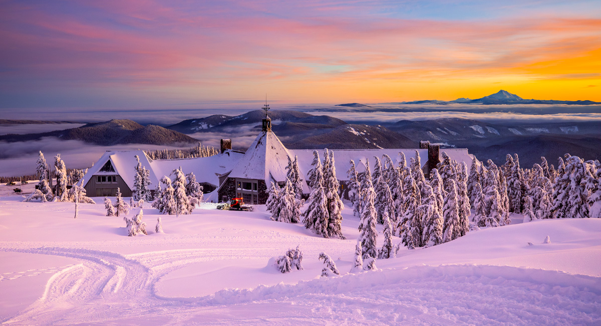 A ski lodge covered in snow with mountain range views.