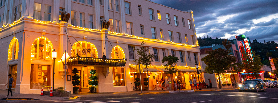 Exterior facade of a hotel. The lower section of building is illuminated with warm string lights.