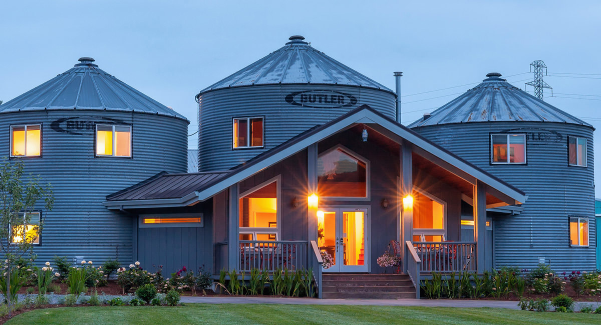 Renovated grain silos at Abbey Road Farm converted into stylish overnight accommodations, warmly lit at dusk with landscaped grounds in front.
