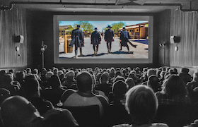 Audience seated in a movie theater watching a film on a large screen.