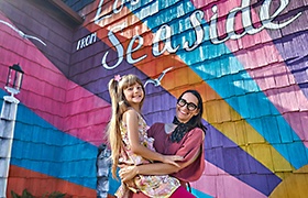 Adult holding a child in front of a colorful mural.