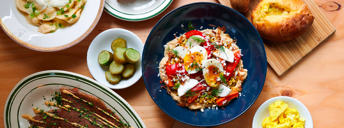 Plates of Slavic food including pickled vegetables, dumplings and a main dish topped with a hard boiled egg.